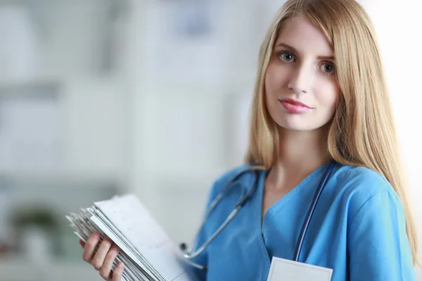 Médico mulher está de pé na janela perto com pasta — Fotografia de Stock