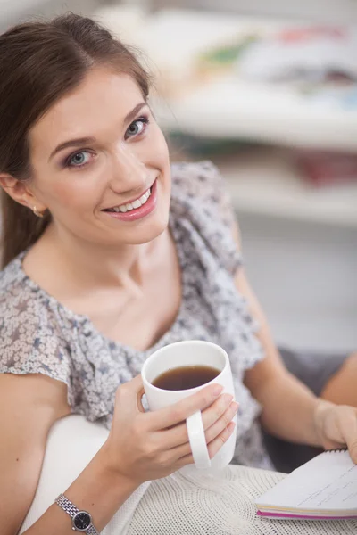 Mujer sentada en el sofá con una taza en las manos — Foto de Stock