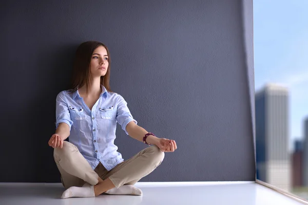 Giovane donna seduta sul pavimento vicino al muro, facendo yoga — Foto Stock