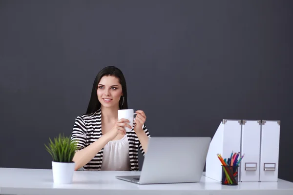 Young woman with a laptop sitting isolated on grey background — Stock Photo, Image