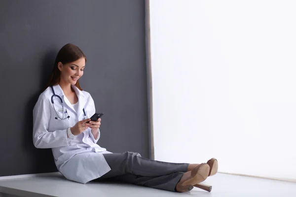 Mujer joven médico sentado en el suelo con su teléfono — Foto de Stock