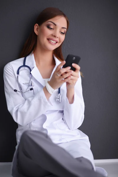 Genç bayan doktor yerde telefonunuzla oturuyor. — Stok fotoğraf