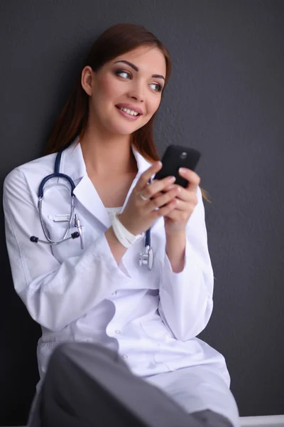 Mujer joven médico sentado en el suelo con su teléfono — Foto de Stock
