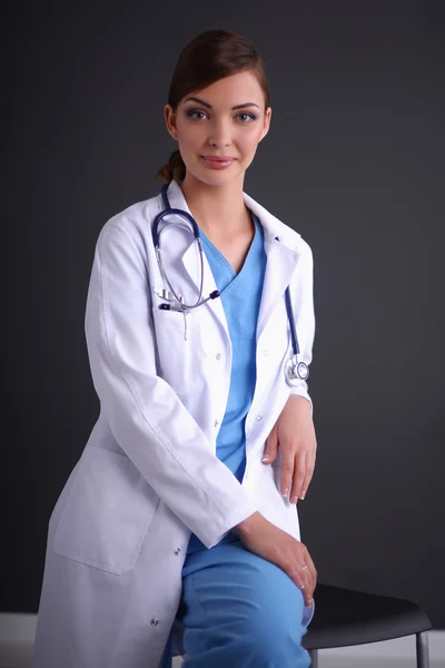 Beautiful female doctor sitting  on stool isolated grey backgro — Stock Photo, Image