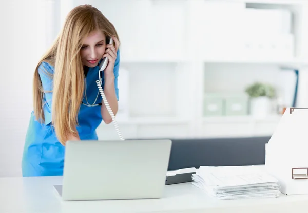 Jovem médico mulher em casaco branco no computador usando telefone — Fotografia de Stock