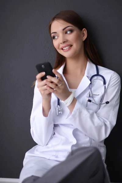 Genç bayan doktor yerde telefonunuzla oturuyor. — Stok fotoğraf