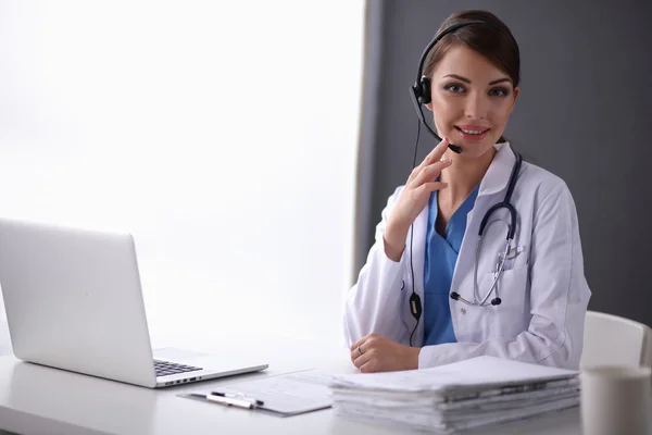 Lekarz w słuchawkach siedzi za biurkiem z laptopem — Zdjęcie stockowe