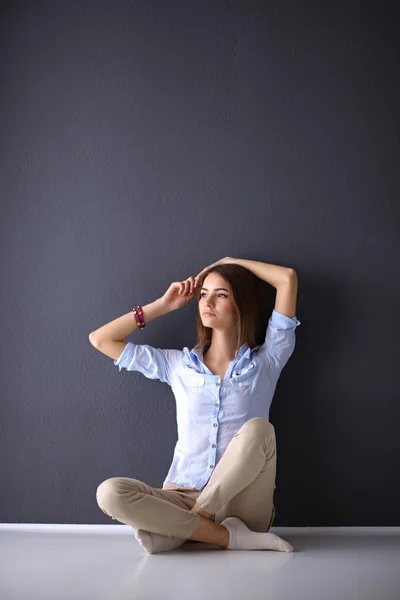 Молодая женщина сидит на полу рядом с темной стеной — стоковое фото