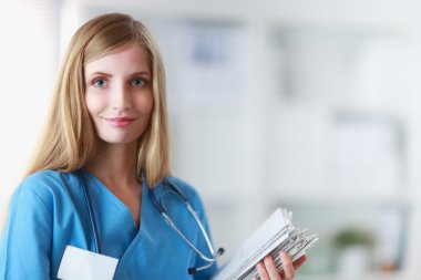 Hastane koridorunda klasörlü kadın doktor portresi.