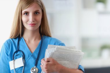 Hastane koridorunda klasörlü kadın doktor portresi.