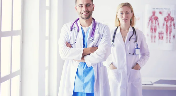 El guapo doctor está hablando con una joven doctora y tomando notas mientras está sentado en su consultorio.. — Foto de Stock