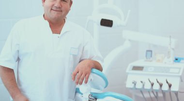 Diş kliniğinde duran gülümseyen bir dişçinin portresi.