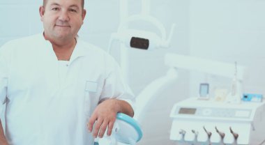 Diş kliniğinde duran gülümseyen bir dişçinin portresi.