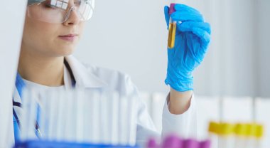 Bir kadın tıbbi veya bilimsel araştırmacı ya da kadın doktor laboratuarda bir test tüpü dolusu temiz çözeltiye bakıyor.