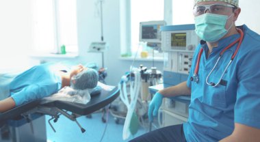 Ameliyat odasında arka planda erkek cerrah var.