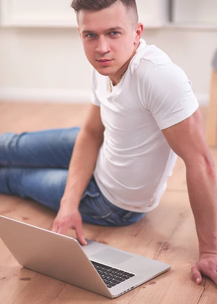 Attractive young man lying on wooden floor and using laptop — Stock Photo, Image