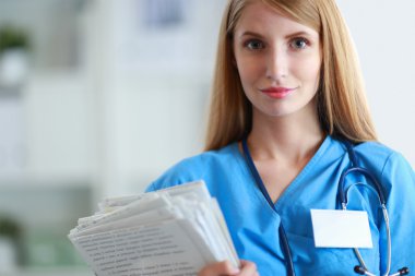 Hastane koridorunda klasörlü kadın doktor portresi.