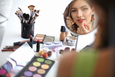 Genç ve güzel bir kadın aynanın yanında makyaj yapıyor.