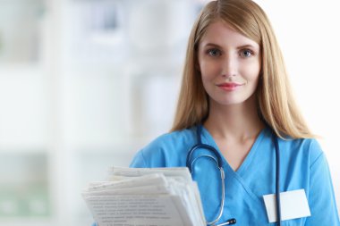 Hastane koridorunda klasörlü kadın doktor portresi.
