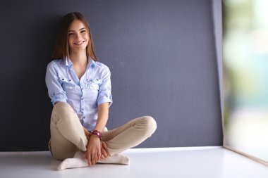 Genç bir kadın yerde, kara duvarın yanında oturuyor.