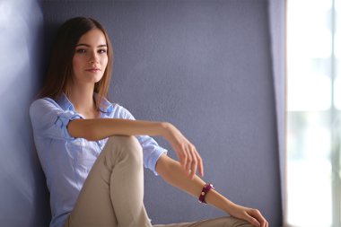 Genç bir kadın yerde, kara duvarın yanında oturuyor.