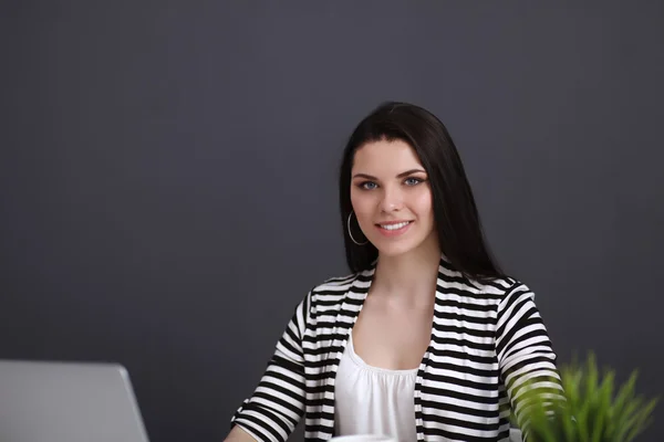 Ung kvinna med en bärbar dator sitter isolerad på grå bakgrund — Stockfoto