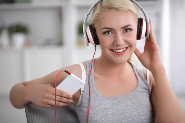 Jonge mooie vrouw thuis zitten op de bank en luisteren muziek — Stockfoto