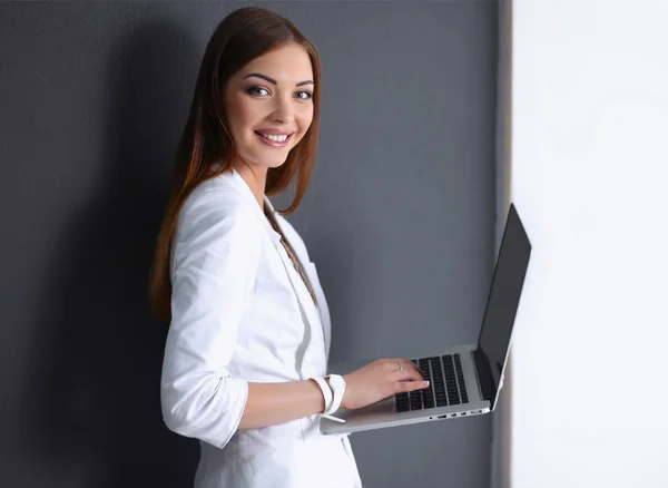Gri arka plan üzerinde izole bir laptop tutan genç kadın — Stok fotoğraf