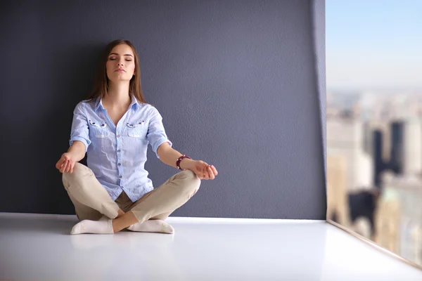 Mladá žena sedící na podlaze u zdi, dělám jógu — Stock fotografie