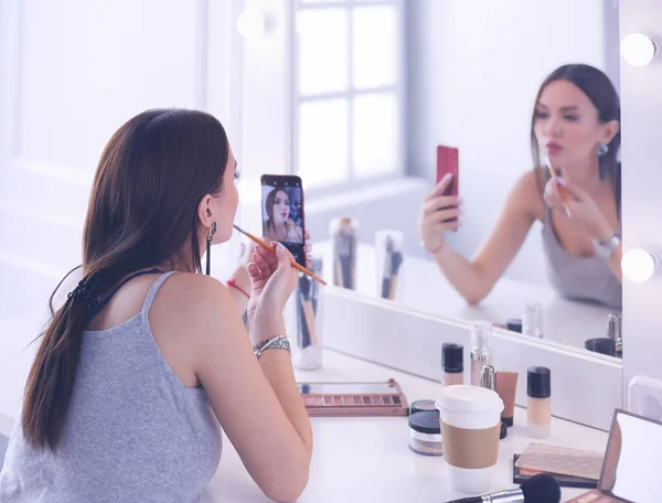 Blogger de belleza filmando tutorial de maquillaje con teléfono inteligente frente al espejo —  Fotos de Stock