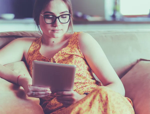 Mladá žena používá tablet při relaxaci doma s kávou na pohovce — Stock fotografie