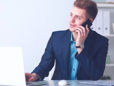 Genç işadamı ofiste çalışıyor, masada oturuyor.