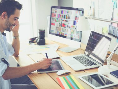 İnternette çalışırken bilgisayarın ve dizüstü bilgisayarın önünde grafik stüdyosunda oturan genç tasarımcının portresi