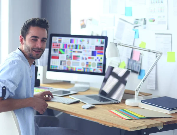 Portrait de jeune designer assis dans un studio graphique devant un ordinateur portable et un ordinateur tout en travaillant en ligne. — Photo