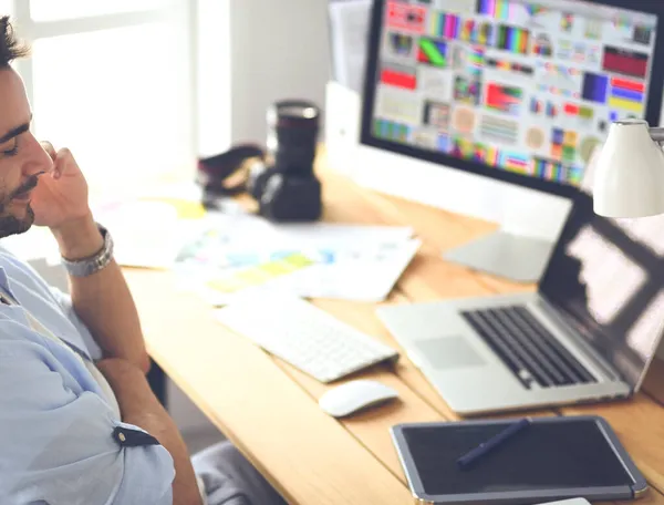 Porträt eines jungen Designers, der im Grafikstudio vor Laptop und Computer sitzt, während er online arbeitet — Stockfoto