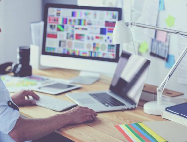 İnternette çalışırken bilgisayarın ve dizüstü bilgisayarın önünde grafik stüdyosunda oturan genç tasarımcının portresi.