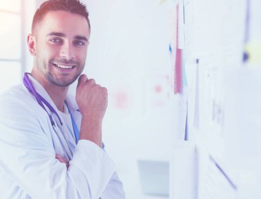 Genç ve kendinden emin erkek doktor portresi tıp ofisinde duruyor..