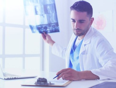 Yakışıklı doktor genç bayan hastasıyla konuşuyor ve ofisinde otururken notlar alıyor..