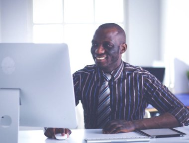 Yakışıklı Afro Amerikalı işadamı Klasik takım elbiseli bir dizüstü bilgisayar kullanarak ve ofiste çalışırken gülümseyen