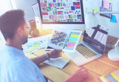 İnternette çalışırken bilgisayarın ve dizüstü bilgisayarın önünde grafik stüdyosunda oturan genç tasarımcının portresi.