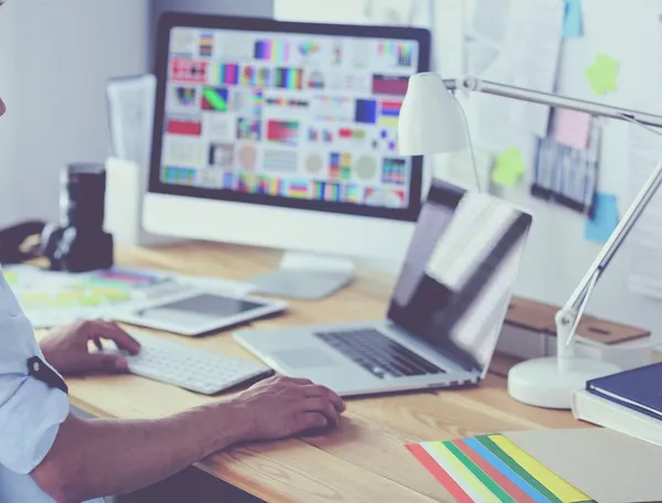 İnternette çalışırken bilgisayarın ve dizüstü bilgisayarın önünde grafik stüdyosunda oturan genç tasarımcının portresi.