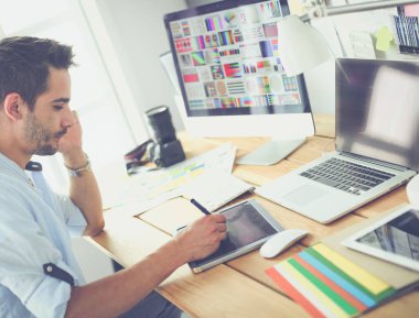 İnternette çalışırken bilgisayarın ve dizüstü bilgisayarın önünde grafik stüdyosunda oturan genç tasarımcının portresi.