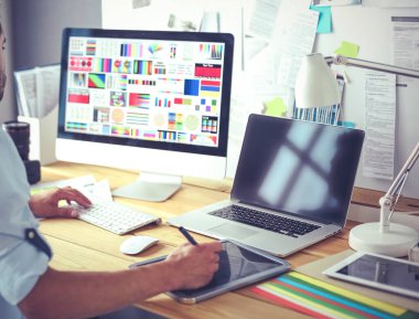 İnternette çalışırken bilgisayarın ve dizüstü bilgisayarın önünde grafik stüdyosunda oturan genç tasarımcının portresi.