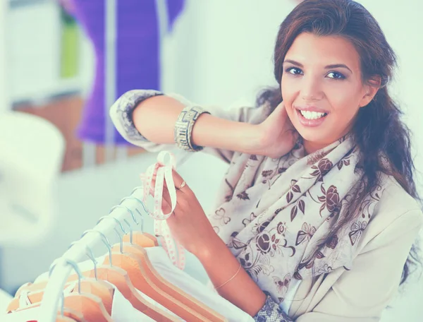 Beautiful young stylist near rack with hangers in office — Stock Photo, Image