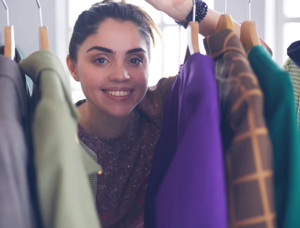 Bonito jovem estilista perto de rack com cabides — Fotografia de Stock