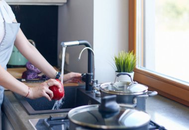 Sebze yıkayan kadın. Güzel genç bir kadın salata için sebze yıkıyor ve mutfakta dururken gülümsüyor.