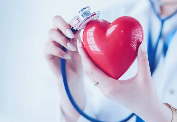 Un médico con estetoscopio examinando el corazón rojo, aislado sobre fondo blanco — Foto de Stock