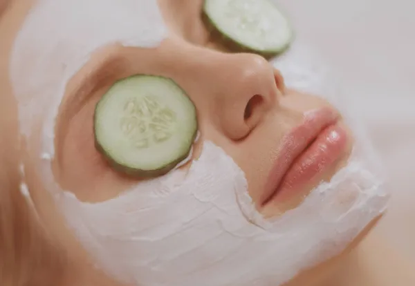 Mooie jonge vrouw ontvangen gezichtsmasker van komkommer in schoonheid salon — Stockfoto