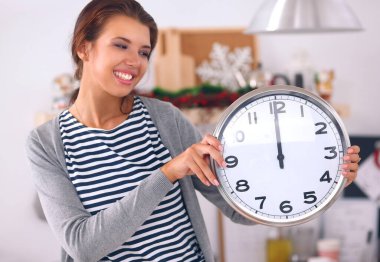Mutlu genç kadın Noel süslemeli mutfakta saat gösteriyor.
