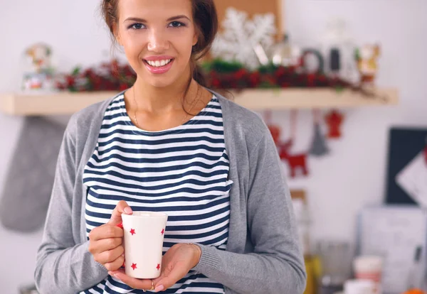 Portret van jonge vrouw met kopje tegen keuken interieur achtergrond. — Stockfoto